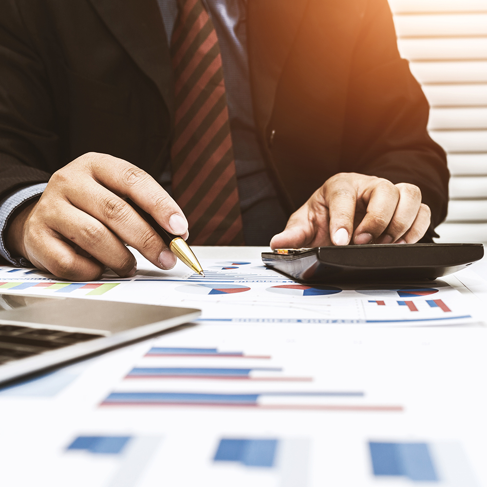 man using calculator with charts on desk